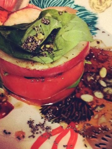 A perfectly stacked tomato and apple tower in a balsamic glaze on a plate with basil