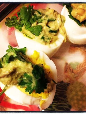 a plate odeviled eggs made with guacamole cut in halves on a plate