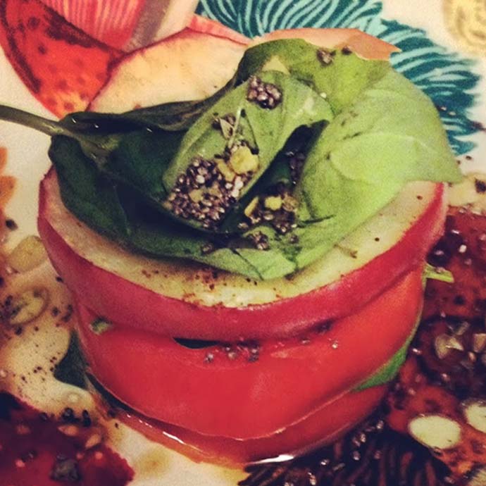 A perfectly stacked closeup of a tomato and apple tower in a balsamic glaze on a plate with basil